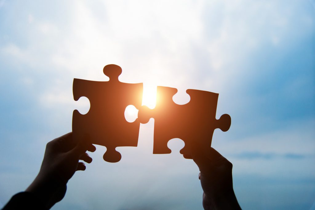 Human hands connecting two jigsaw puzzle pieces against cloudy sky